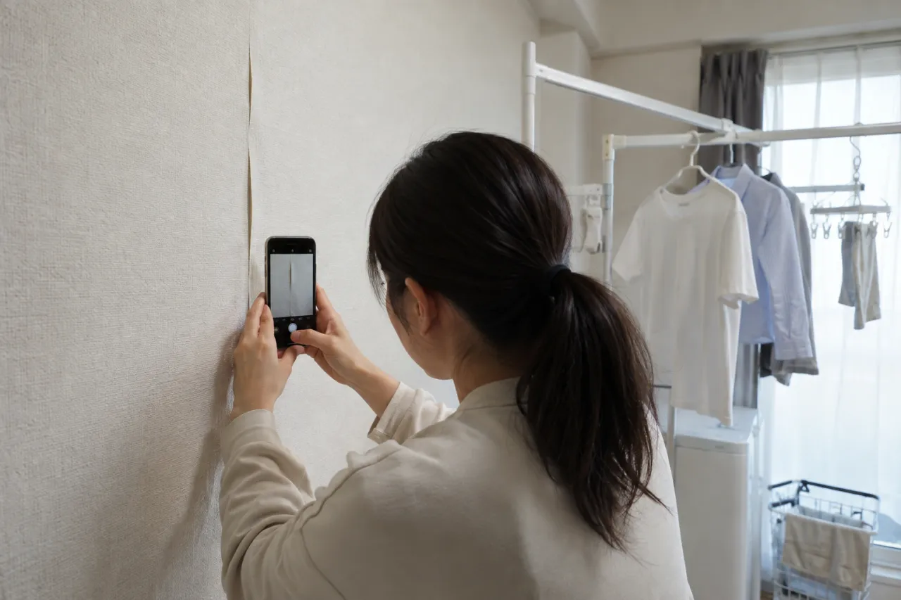 室内干しの近くの壁をスマートフォンで記録する入居者