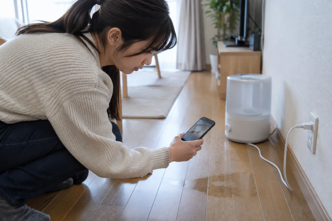 加湿器のそばで濡れた床を確認する入居者